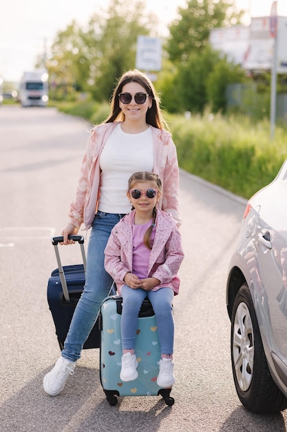 Adorable petite fille est assise sur sa valise pour enfant et attend le voyage avec sa maman deux belles