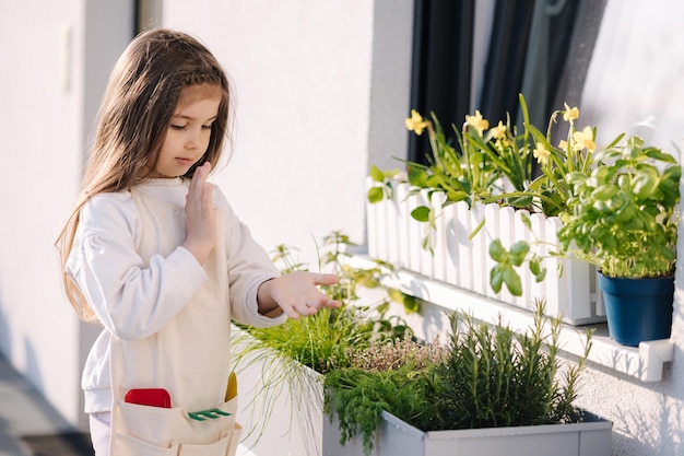 Adorable petite fille goûte les verts frais de son parterre de fleurs sous la fenêtre du balcon