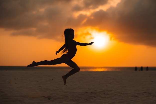 Adorable petite fille heureuse sur la plage blanche au coucher du soleil.