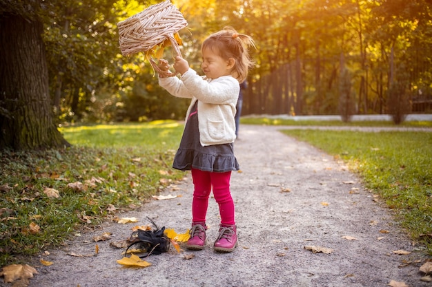 Adorable petite fille jouant à l'automne ensoleillé prak jolie petite fille verse des feuilles jaunes d'automne d'un