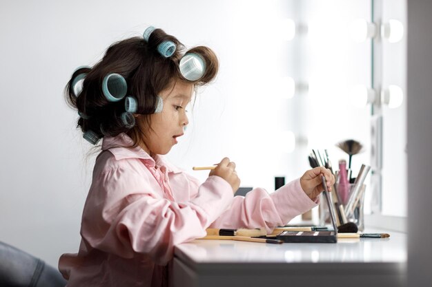 Adorable petite fille jouant avec le cosmétique de sa mère devant le miroir à la maison