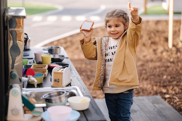 Adorable petite fille jouant dans la cuisine de jouets à l'extérieur jolie fille de trois ans s'amuser dans la ville des enfants