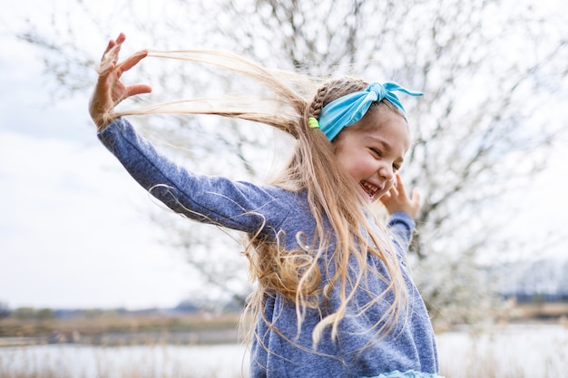 Adorable petite fille jouant dans un jardin de pommiers en fleurs à la chasse aux œufs de Pâques, courant et souriant. Enfant dans un verger de printemps avec des fleurs de cerisier.