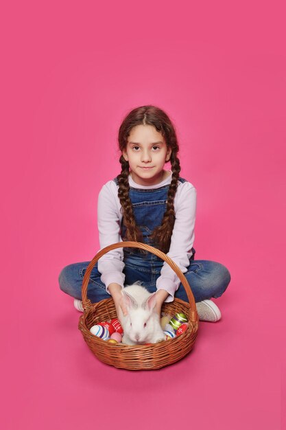Adorable petite fille joue avec ses lapins en regardant la caméra isoaltée sur un fond rose Concept de Pâques