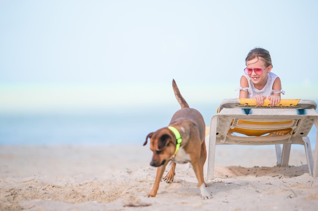 Adorable petite fille sur la plage jouant avec un chien