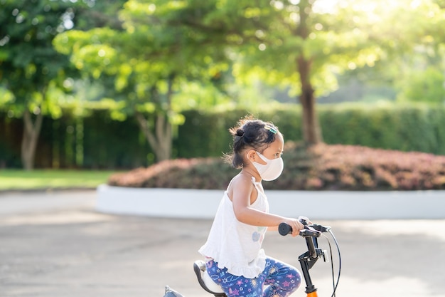 Adorable petite fille portant un masque protecteur faisant du vélo au parc