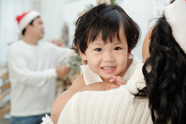 Adorable petite fille positive dans les mains de la mère en bonnet de Noel