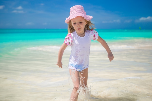 Adorable petite fille qui court dans l'eau peu profonde à la plage exotique