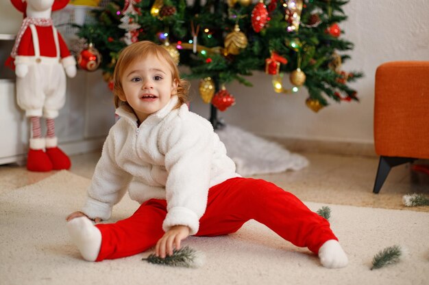 Photo une adorable petite fille qui s'amuse sur un tapis doux devant un arbre de noël