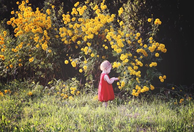 Adorable petite fille en robe rouge vif marchant dans le parc d'été avec des fleurs de rudbeckia dorées