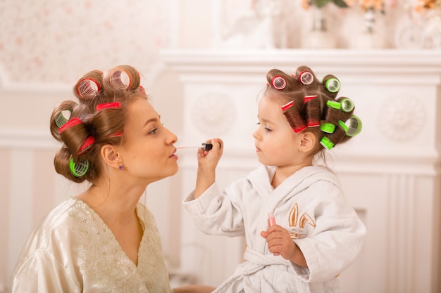 Adorable petite fille avec sa mère en bigoudis appliquer le maquillage. Maman apprend à sa fille à utiliser des cosmétiques. Journée beauté. Les filles sont de telles filles.