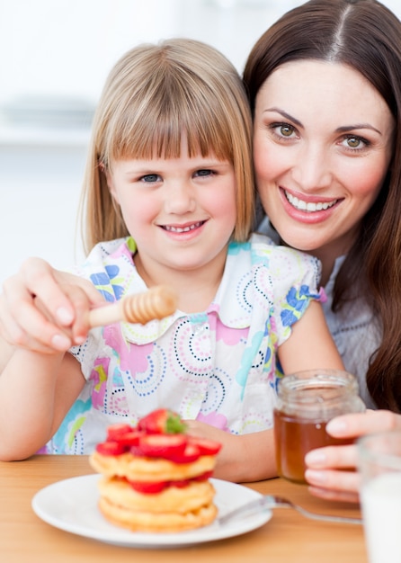 Adorable petite fille et sa mère mettant du miel sur des gaufres