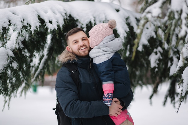 Adorable petite fille avec son adorable papa se tient près du grand arbre enneigé