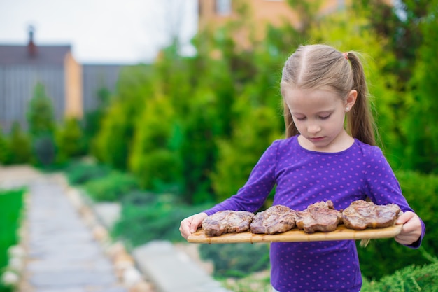 Adorable petite fille avec des steaks grillés dans les mains en plein air