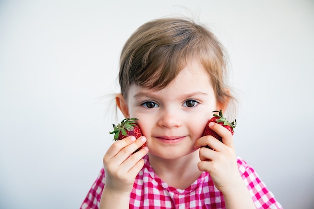 Adorable petite fille tenant deux grosses fraises