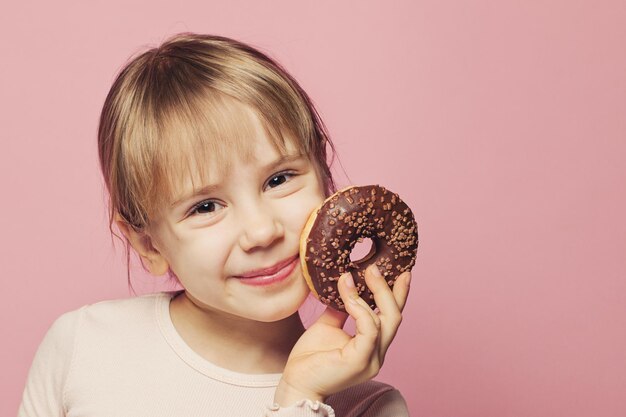 Une adorable petite fille tenant un donut au chocolat sur un fond rose