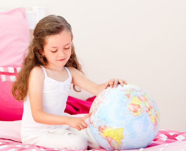 Adorable petite fille tenant un globe terrestre assis sur son lit