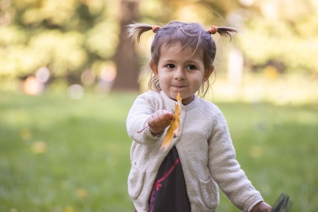 Adorable petite fille tend une feuille d'érable jaune d'automne dans l'appareil photo