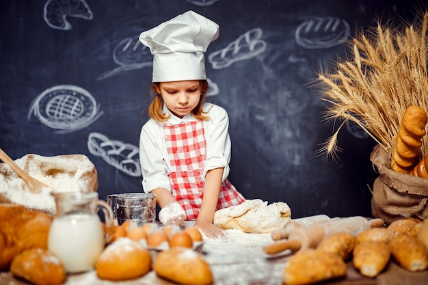 Adorable petite fille en toque faisant la pâte