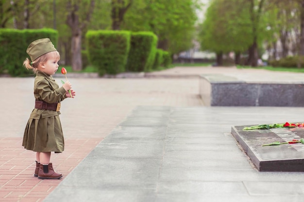 Adorable petite fille en uniforme militaire soviétique dépose une fleur sur un monument à ceux qui ont été tués dans le monde W