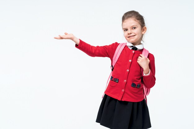 Adorable petite fille en veste d'école rouge, robe noire, sac à dos pointant