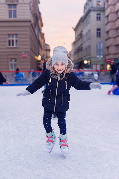 Photo adorable petite fille en vêtements d'hiver et bonnet pompon patinant sur la patinoire