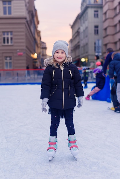 Adorable petite fille en vêtements d'hiver et bonnet pompon patinant sur la patinoire