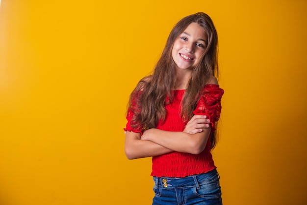 Adorable petite pré adolescente sur fond jaune souriante avec les bras croisés.