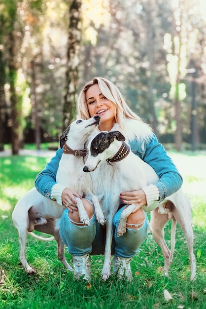 adorable propriétaire de femme blonde heureuse avec ses deux whippets blancs en plein air