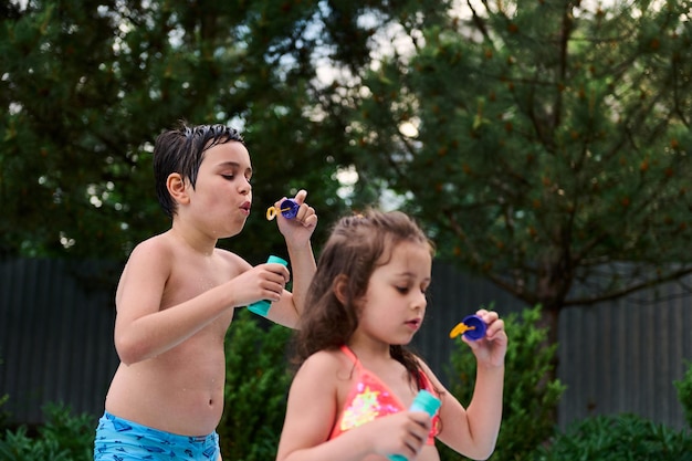 Adorables enfants soufflent des boules de savon tout en s'amusant dans la piscine gonflable du jardin de la maison Loisirs d'été