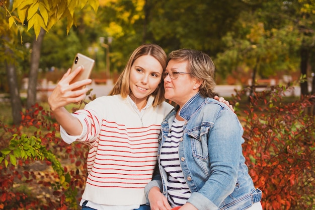 Adorables femmes maman et fille sont assises sur un banc dans un magnifique parc d'automne et prennent un selfie au téléphone