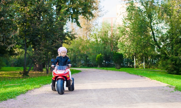 Adorables petites filles à cheval sur la moto pour enfants dans le parc verdoyant