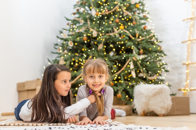 Adorables petites filles près d'un arbre de Noël dans un salon confortable en hiver