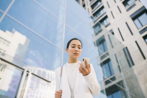 Photo adulte asiatique belle femme avocate marche devant le centre de bureau à la recherche sur son téléphone portable en lisant le massage du client