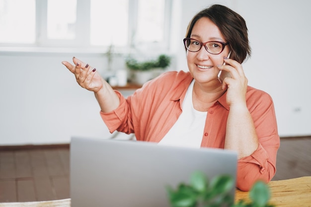 Adulte charmante femme brune dans des verres plus un corps de taille positive travaillant avec un ordinateur portable au bureau à domicile