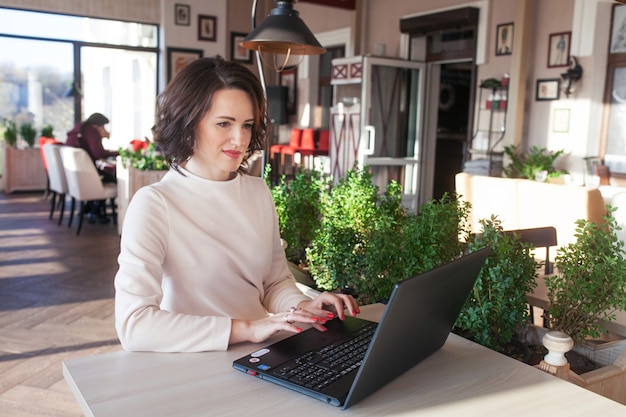 Adulte élégante femme d'affaires en robe blanche, assis avec un ordinateur portable au café. Belle dame brune à l'aide de cahier au café. Photo d'une femme d'âge moyen tapant sur le clavier