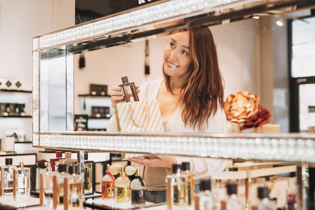 Adulte jolie femme souriante aux cheveux noirs dans le magasin de cosmétiques et de parfums magasinage de vacances