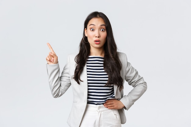 Affaires, finances et emploi, concept féminin d'entrepreneurs prospères. Une femme asiatique surprise et intriguée travaillant au bureau entend parler d'une promo intéressante et pointant vers la gauche curieuse