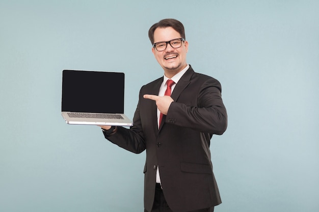 Affaires, gadgets, technologies. Homme d'affaires pointant sur l'ordinateur portable du moniteur. Intérieur, tourné en studio, isolé sur fond bleu clair ou gris