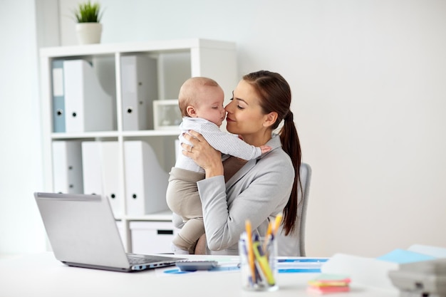 affaires, maternité, multitâches, famille et concept de personnes - femme d'affaires heureuse et souriante avec bébé et ordinateur portable travaillant au bureau