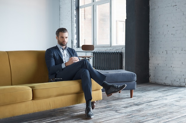 Les affaires ont l'air réussies et un bel homme d'affaires est assis sur un canapé de bureau et regarde de côté