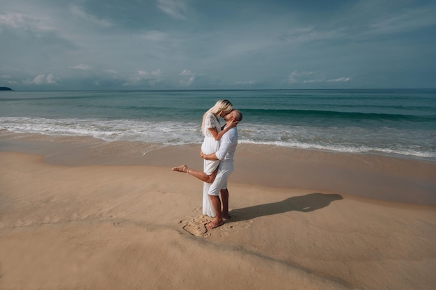 Affectueusement embrassé et tendrement embrassé, un jeune couple en vêtements blancs profite d'une journée d'été sur une plage de sable humide. Phuket, Thaïlande.