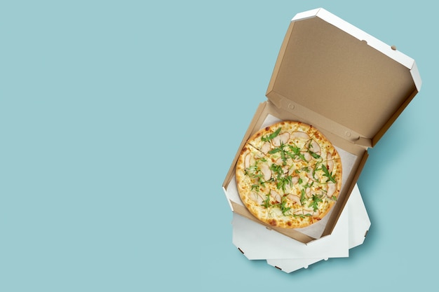 Photo affiche conceptuelle pour la livraison de nourriture et de pizza. pizza à la viande dans une boîte en carton pour livraison sur une surface bleue avec place pour le texte