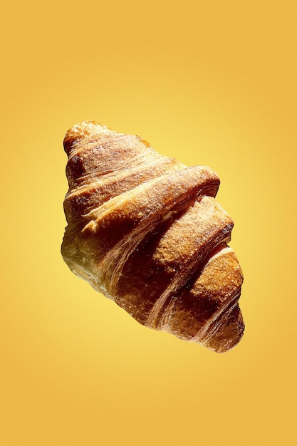 Une affiche avec un croissant en lévitation sur fond jaune. Croissant fraîchement sorti du four pour le petit déjeuner.