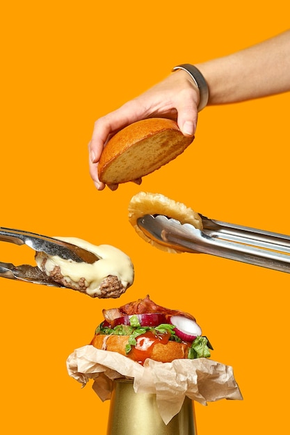 Affiche de cuisine de hamburger. Les mains mettent la côtelette, le petit pain et l'ananas sur le petit pain. Affiche créative avec tempête volante