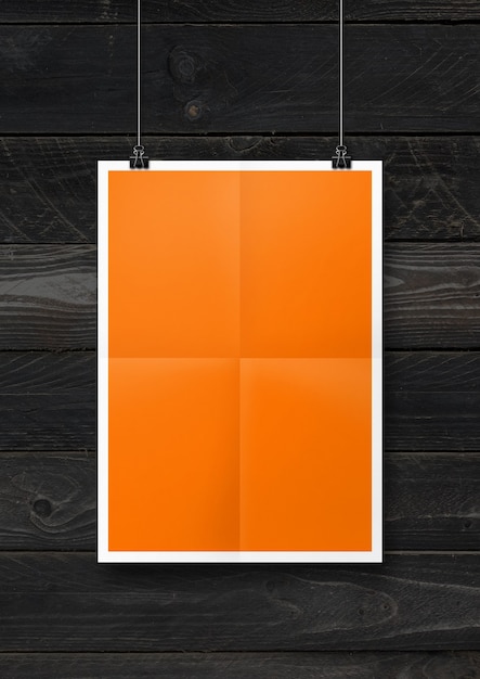 Affiche pliée orange accrochée à un mur en bois noir avec des clips. Modèle de maquette vierge