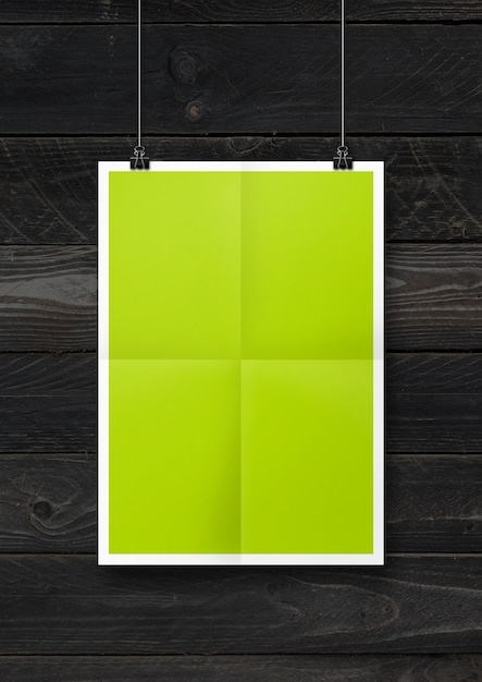 Affiche pliée vert citron accrochée à un mur en bois noir avec des clips.