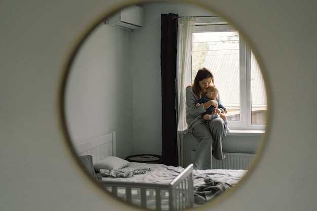 Afficher dans le miroir comment une mère joue avec son enfant. Maman d'un bébé allaité. Bonne maternité. La famille est à la maison. Portrait d'une mère et d'un enfant heureux.