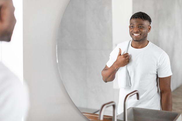 Un Africain avec une serviette sur l'épaule regarde dans le miroir de la salle de bain.