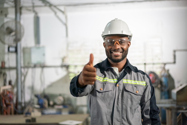 African American male ingénieur en uniforme souriant et montrant les pouces vers le haut à fa industriel